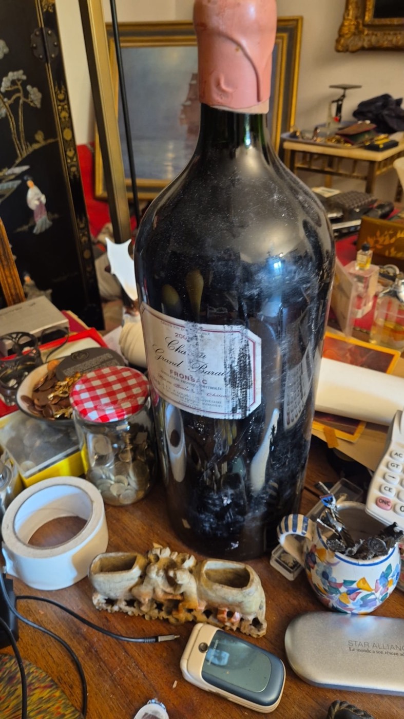 Grande bouteille ancienne de vin de Bordeaux, appellation Fronsac, posée parmi des pièces et objets anciens