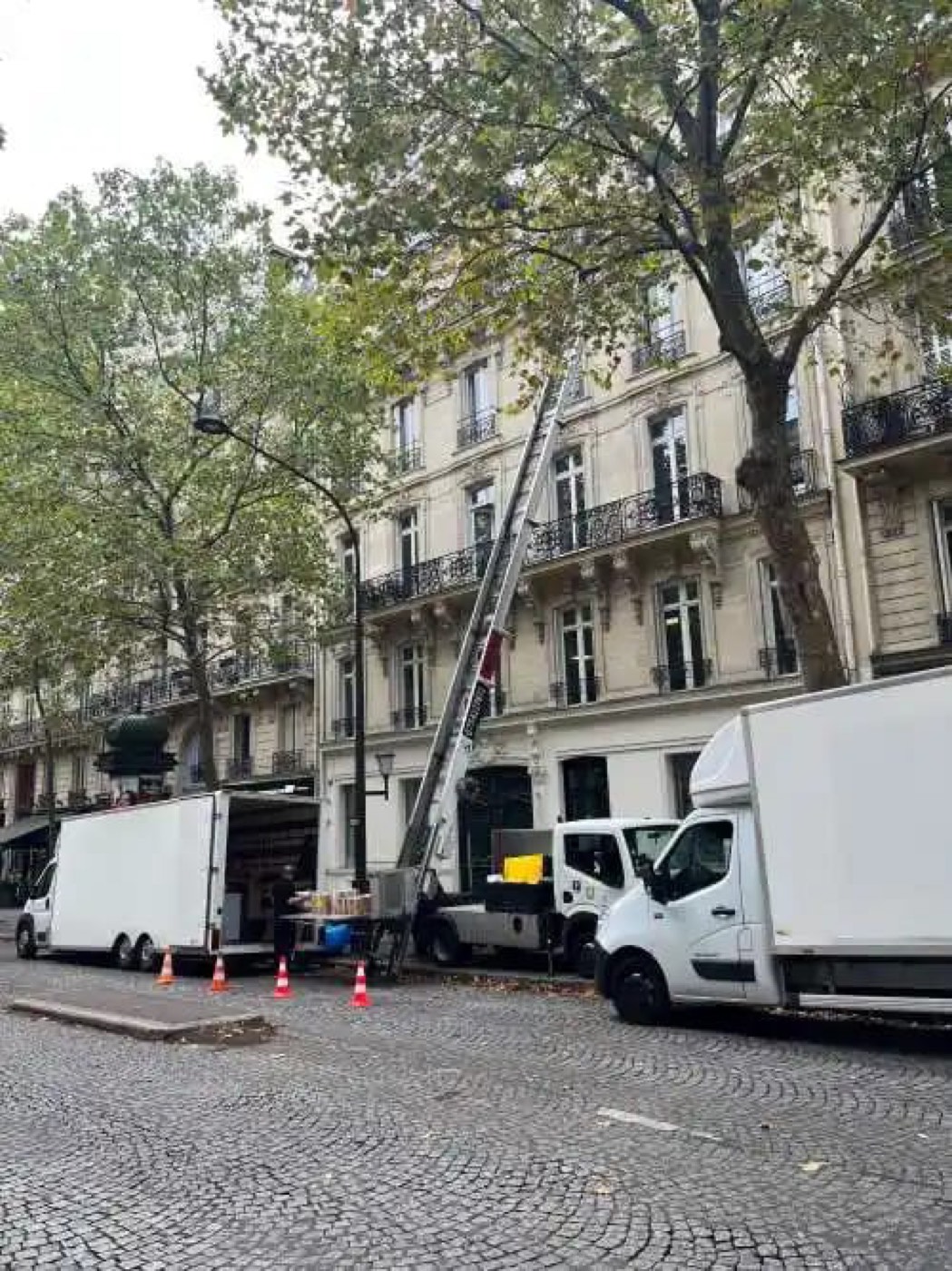 Deux camions de déménagement et un monte-meuble devant un immeuble haussmannien lors d'un débarras