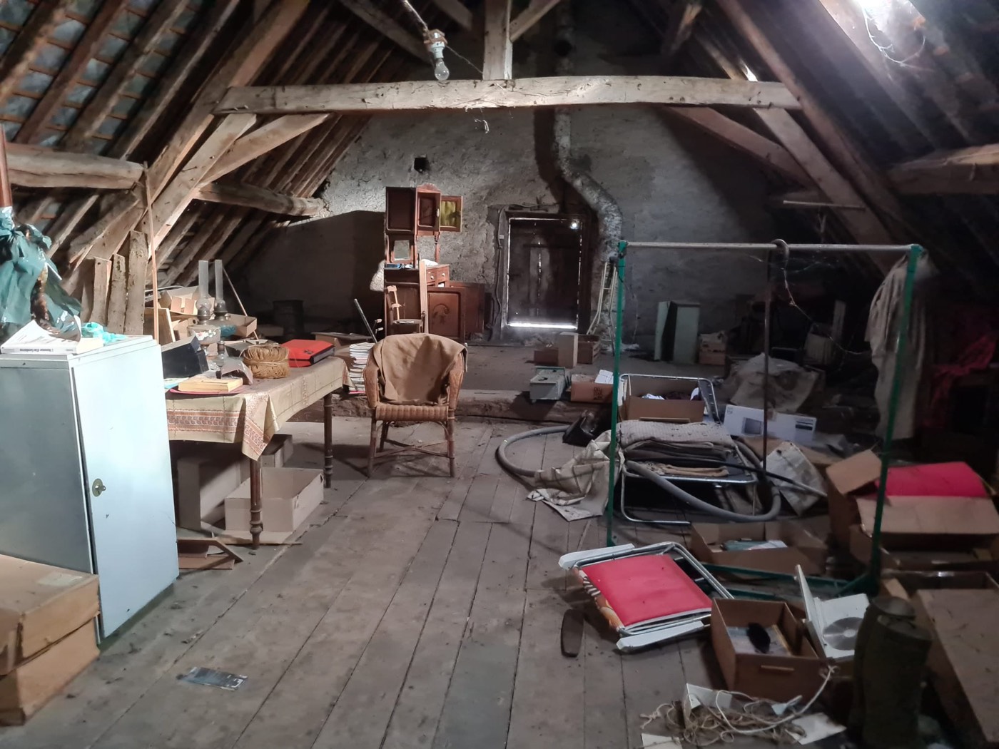 Mobilier ancien et objets divers entassés dans un grenier poussiéreux avant enlèvement et débarras.