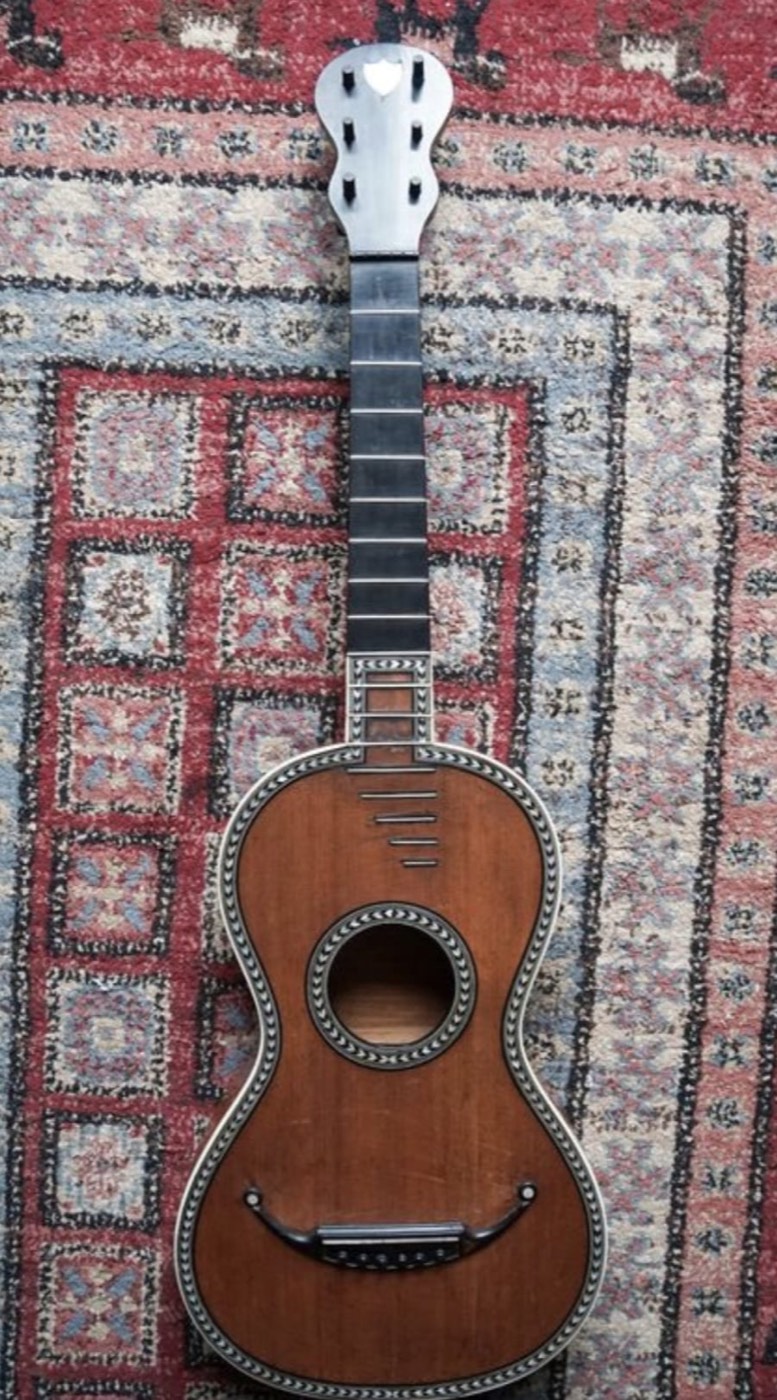 Guitare romantique ancienne en bois à filets décoratifs posée sur un tapis oriental
