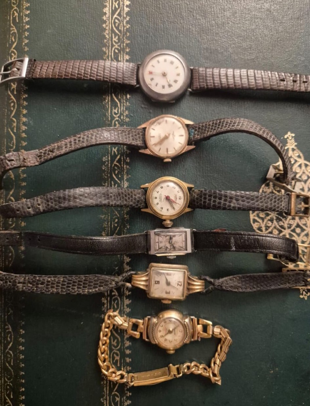 Lot de six montres-bracelets anciennes pour dame, boîtiers dorés et bracelets en cuir, posées sur une reliure ancienne.