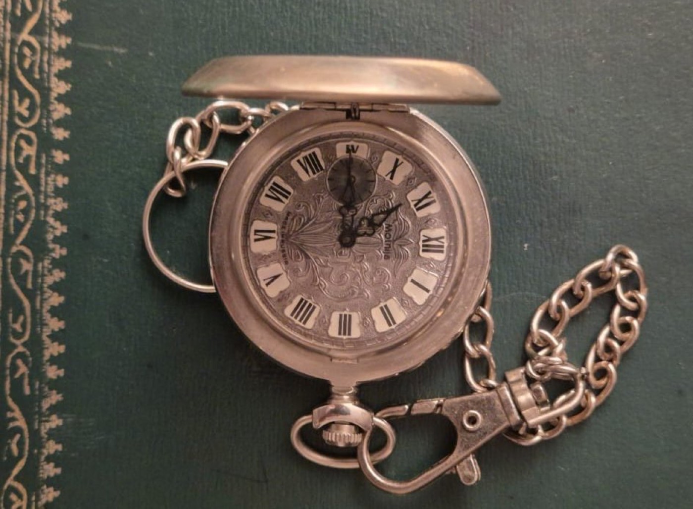 Montre de gousset ancienne à couvercle, cadran gravé et chiffres romains, avec sa chaîne en métal argenté.