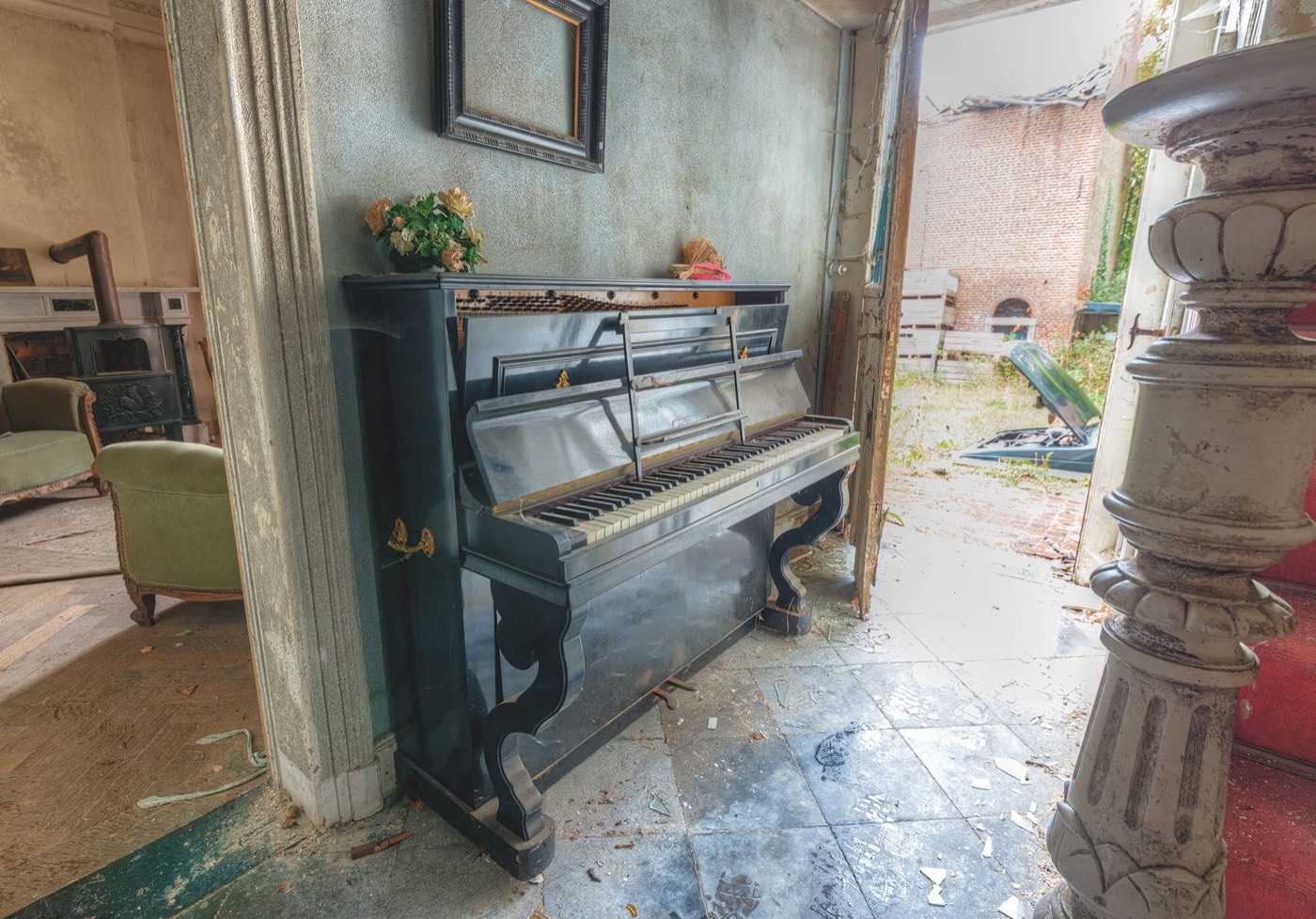 Piano droit ancien laqué noir abandonné dans une demeure délabrée aux carreaux brisés.