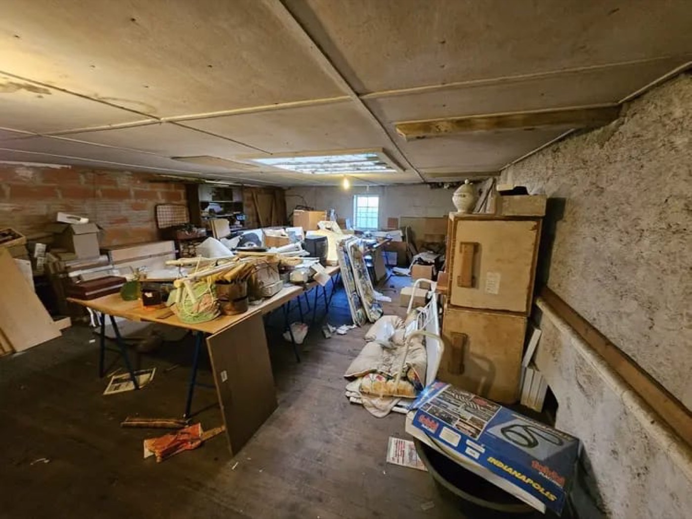 Sous-sol encombré de cartons, meubles et objets divers à débarrasser dans une cave ancienne.