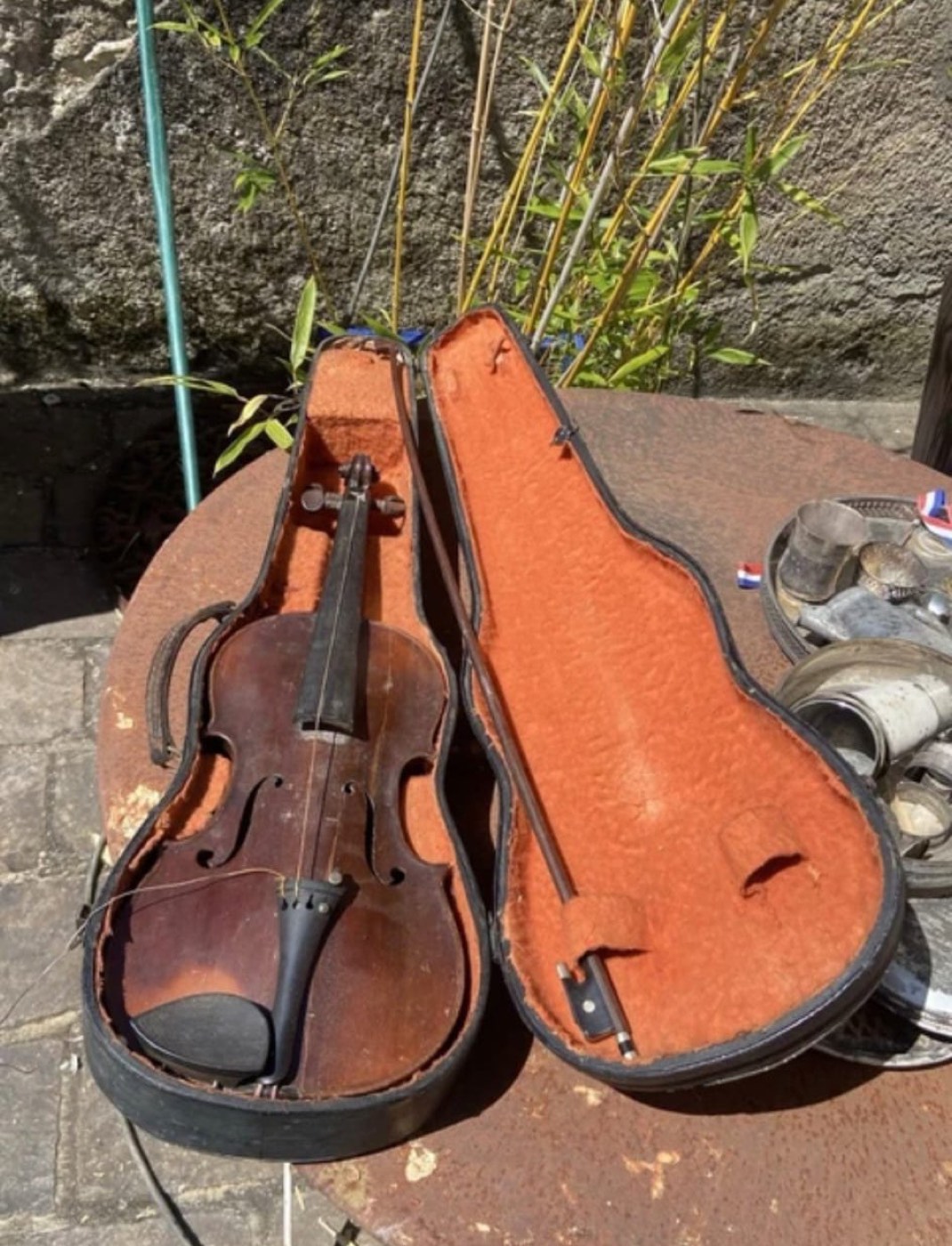 Violon ancien et son archet dans un étui ouvert, présentés en extérieur près d'argenterie